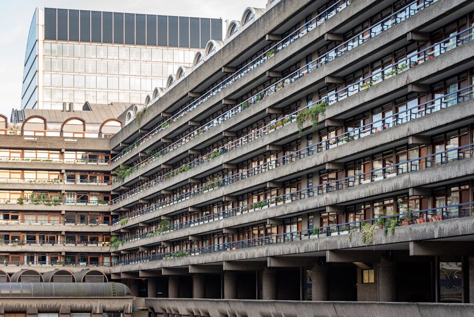 A multi-storey residential building with a brutalist architectural style, featuring horizontal concrete slabs creating distinct balconies for each apartment. The balconies are lined with metal railing